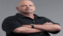 a bald man with his arms crossed wearing a black shirt