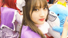 a woman in a purple dress is holding a stuffed shark and looking at the camera .