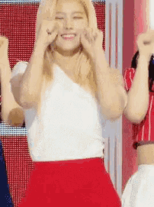 a woman in a white top and red skirt is dancing on a stage with her hands in the air .