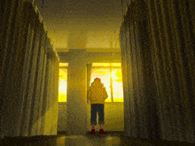 a man in a yellow hoodie stands in a hallway looking out of a window