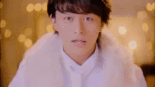 a man wearing a white fur coat and a white shirt is looking at the camera .