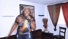 a man singing into a microphone in a living room wearing a pink floyd shirt