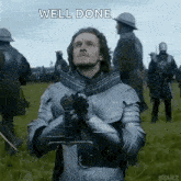 a man in armor is holding a sword in front of a crowd of men .