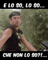 a man wearing a headband stands next to a motorcycle with the words e lo so lo so che non lo so