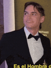a man in a suit and bow tie stands in front of a sign that says miyake sey