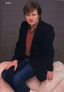 a man in a black jacket is sitting on a pink blanket with the name jones written above him
