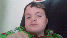 a young boy wearing a green and red christmas sweater looks tired