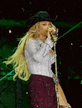 a woman wearing a cowboy hat is singing into a microphone on a stage