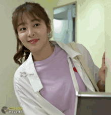 a woman wearing a white coat and a purple shirt is standing next to a wall with yoyo.kr written on it