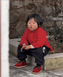 a little girl wearing a red shirt and black pants is squatting