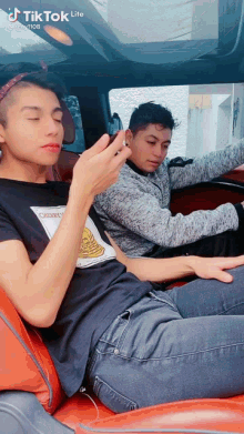 two young men are sitting in a car with tik tok lite written on the bottom right