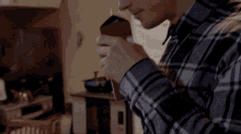 a man in a plaid shirt is drinking from a mug