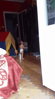 a little girl in a diaper stands on a wooden floor in a living room