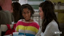 two girls are sitting at a table with a netflix logo in the background