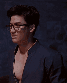 a young man wearing glasses and a blue jacket is standing in a dark room