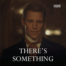 a man in a suit and tie is standing in front of a sign that says " there 's something "