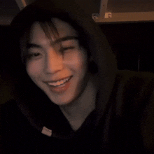 a young man wearing a black hoodie is smiling with his hand in his mouth .