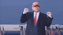 donald trump wearing a make america great again hat stands in front of an airplane