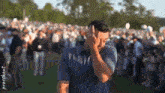 a man is standing in front of a crowd on a golf course and covering his face with his hand .