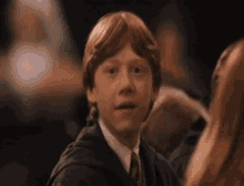 a young boy with red hair is wearing a green robe and tie and making a funny face .