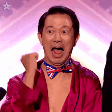 a man wearing a bow tie and a pink robe holds his fist in the air