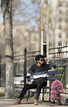a man wearing sunglasses sits on a bench next to a pink flower
