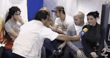a group of people are sitting around a man holding a microphone and talking to him .
