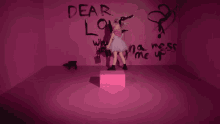 a girl in a pink dress is standing in front of a pink wall that has dear love written on it