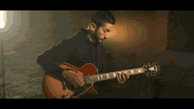 a man in a black shirt is playing a guitar with a sticker on it that says ' gibson '