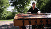 a woman is playing a wooden xylophone in a park with trees in the background ..