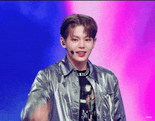 a young man wearing a silver jacket and a black shirt is standing on a stage with a microphone in his mouth .