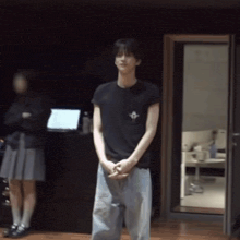 a man in a black shirt is standing in a dark room with his hands folded