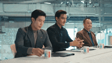 three men are sitting at a table with coffee mugs that say mcdonalds on them