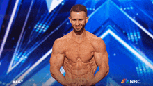 a shirtless man stands in front of a blue background with the nbc logo on it