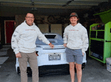 two men standing in front of a car with a texas license plate that says gstryor