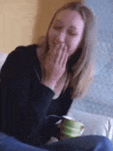 a woman covering her mouth with her hands while holding a green cup