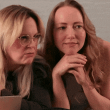 two women sitting next to each other with their hands on their chins