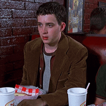 a man in a brown jacket sits at a table with a bag of french fries