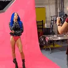 a woman with blue hair stands in front of a pink background
