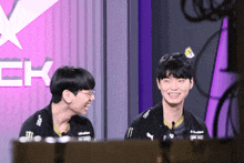 two young men are smiling in front of a sign that says ' ck ' on it