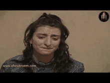 a woman is crying and making a funny face while sitting in front of a wall .