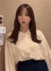 a woman in a white shirt and black skirt is standing in front of a wall and looking at the camera .