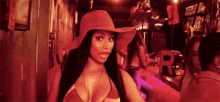 a woman wearing a bikini and a hat is standing in a dark room .