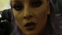 a close up of a woman 's face with purple hair making a funny face .