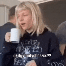 a woman is drinking a cup of coffee while wearing a hoodie .