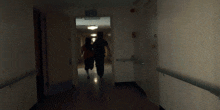 a man and a woman are running down a hallway with an exit sign in the corner