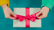 a person is tying a pink bow on a white gift box