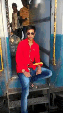 a man in a red shirt is sitting on the steps of a bus