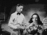 a man in a bow tie stands next to a woman eating a sandwich