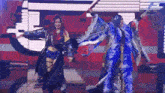 a couple of women are dancing on a stage and one is wearing a blue feathered outfit .